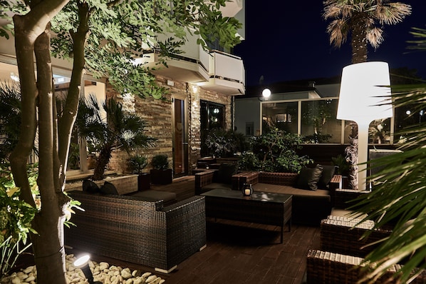 Un espace extérieur aménagé en terrasse, avec des meubles en osier, une grande table et un lampadaire.