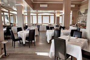 Un comedor amplio con varias mesas dispuestas para comer, ventanas grandes que proporcionan luz natural y un diseño interior moderno.