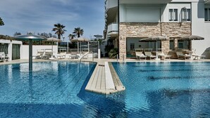 A swimming pool with lounge chairs and umbrellas, surrounded by a modern building with stone accents. - Rouge Hotel International (Cervia)