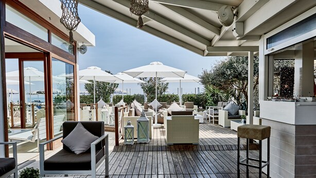 A covered outdoor seating area with wicker furniture, white umbrellas, and a view of the sea. - Rouge Hotel International (Cervia)