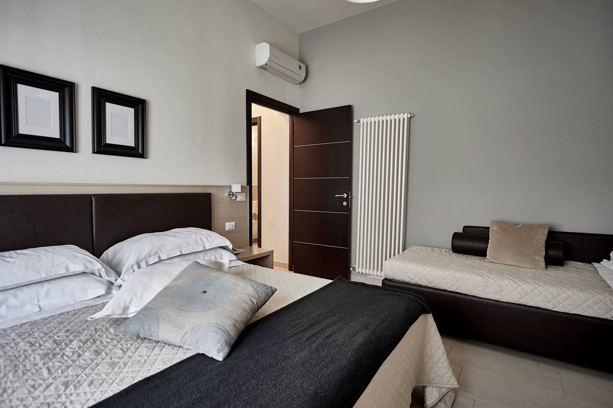 Une chambre d’hôtel avec deux lits, une armoire, un radiateur et des tableaux encadrés au mur.