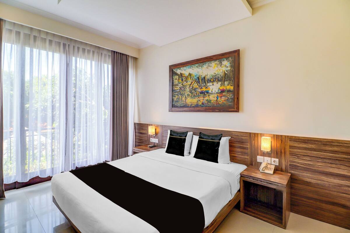 Una habitación de hotel con una cama grande, un cuadro en la pared y una ventana con cortinas.