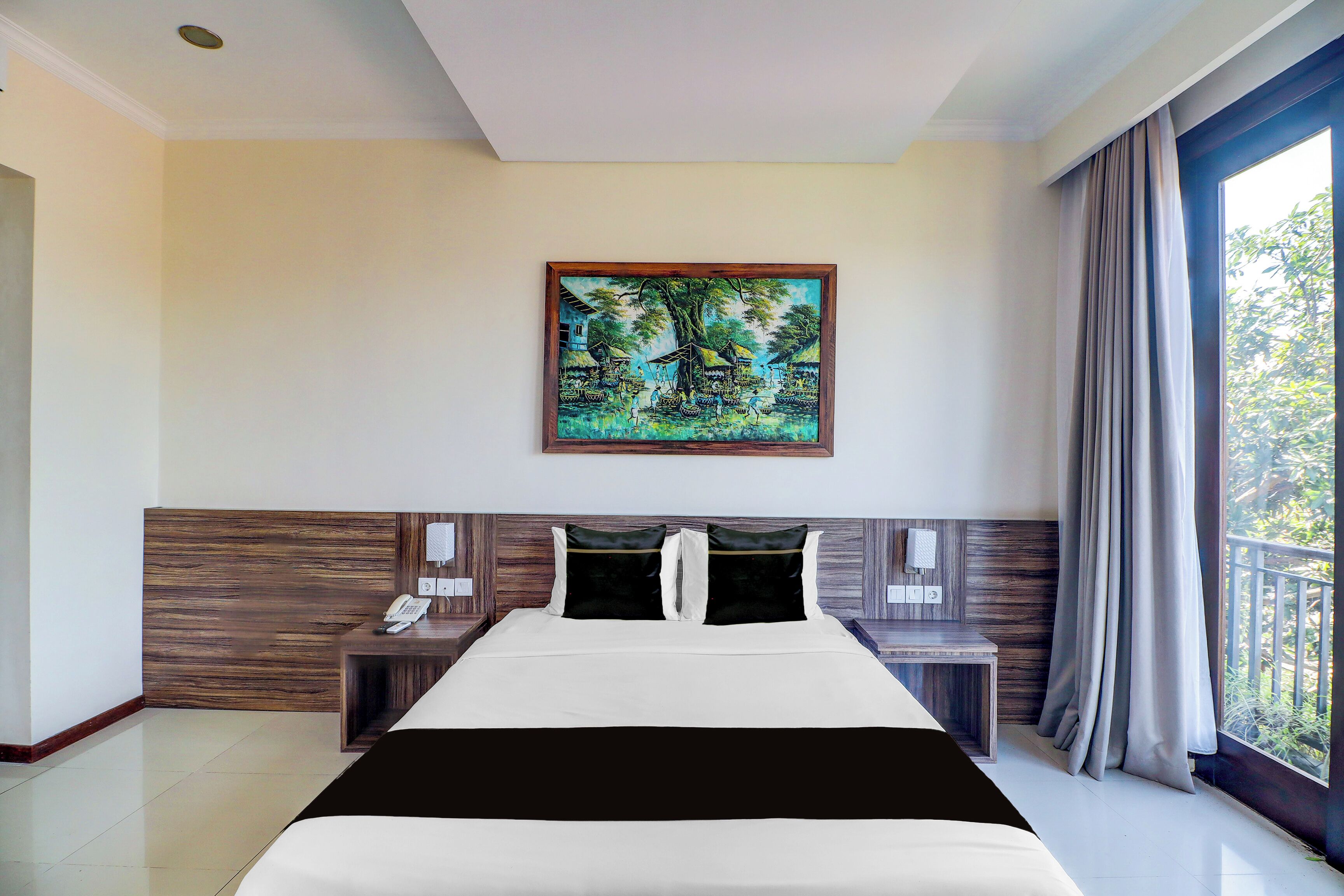A hotel room with a bed, a painting on the wall, a nightstand, and a window with curtains.