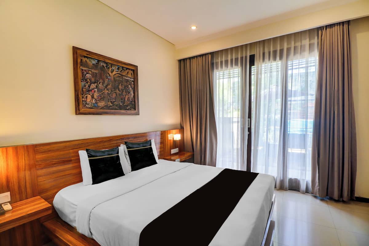 Habitación de hotel con una cama grande, una mesita de noche, un cuadro colgado en la pared y un ventanal con cortinas.