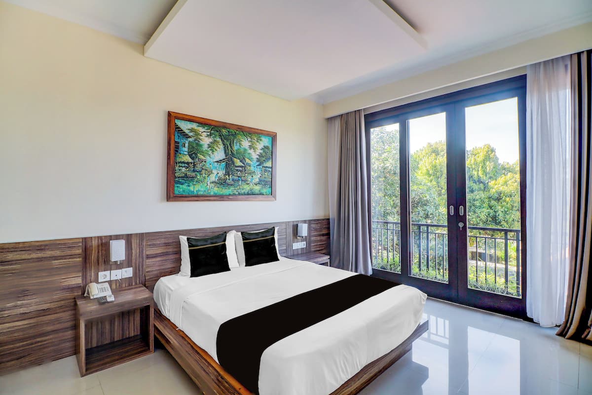 Una habitación de hotel con una cama grande, un cuadro, un teléfono y un balcón con cortinas.