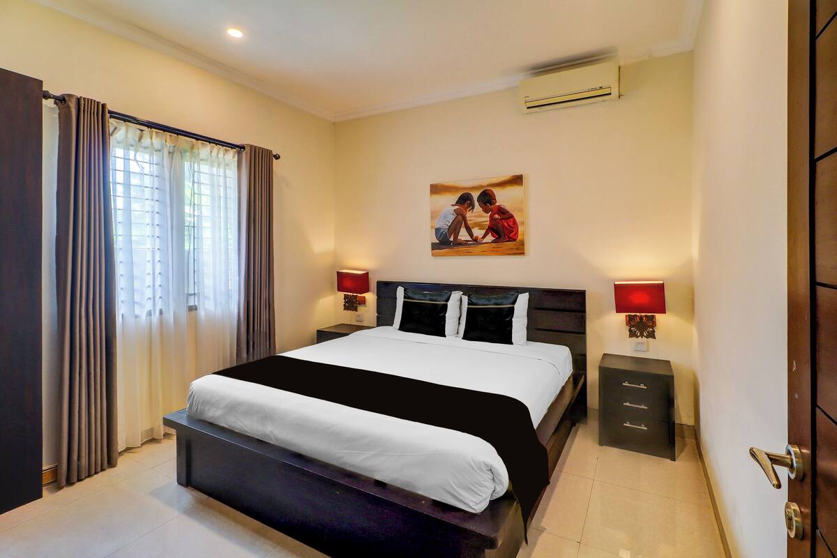 Una habitación de hotel con cama, mesitas de noche, aire acondicionado en la pared y un cuadro.