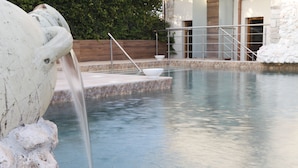 A stone fountain with water flowing into a pool, surrounded by a wooden deck and a white wall. - Hotel Villa Clementina (Scafati)