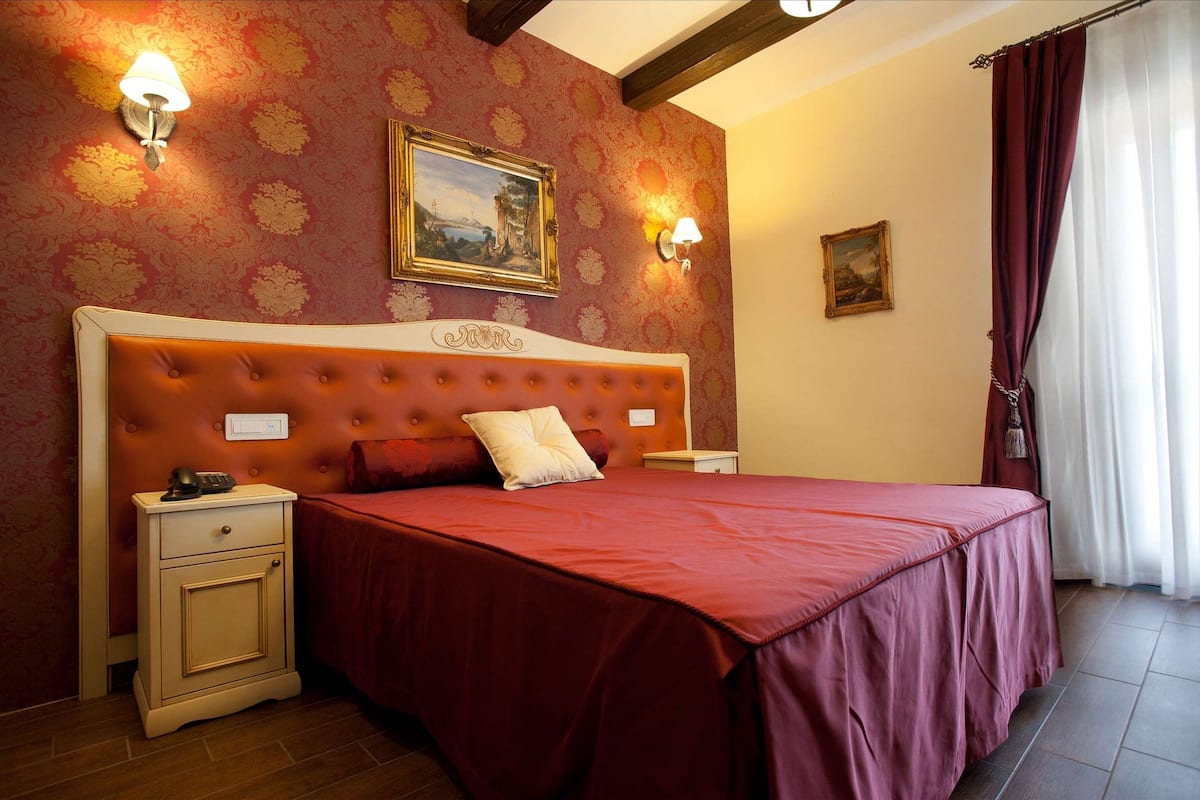 Une chambre à coucher avec un grand lit, deux tables de chevet, une petite table et une lampe fixée au mur.