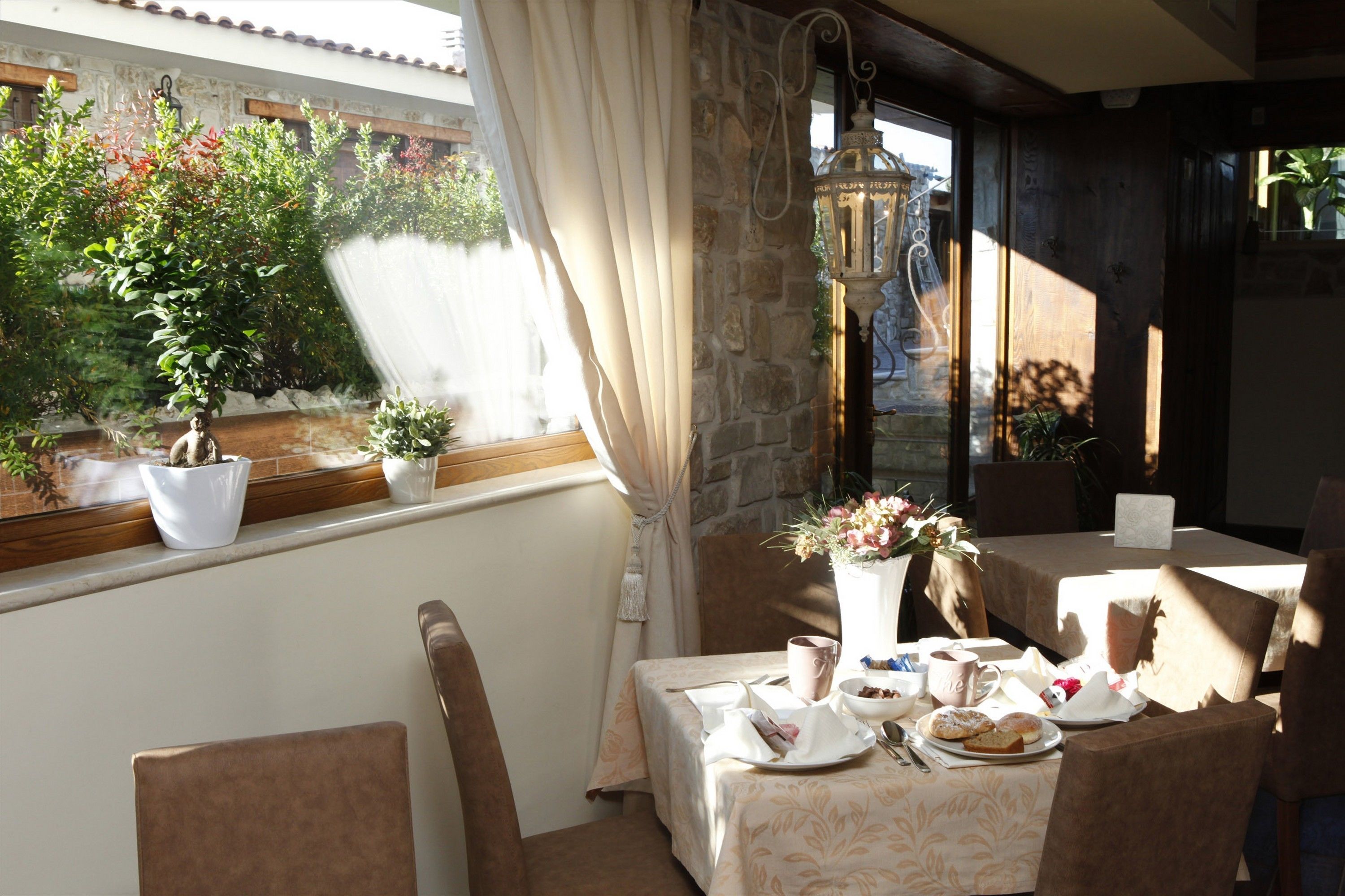 A dining area with a table set for two, potted plants, and a stone wall.
