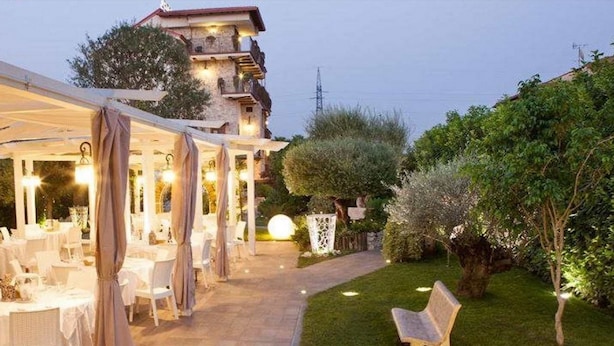 An outdoor dining area with tables and chairs, a pathway, and a building in the background. - Hotel Villa Clementina (Scafati)