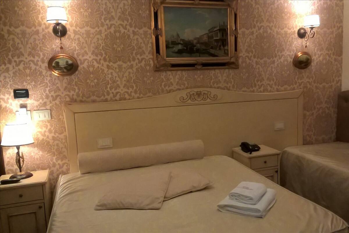 Une chambre d’hôtel avec un grand lit, une table de chevet avec une lampe, une autre table de chevet avec un téléphone et un tableau au mur.