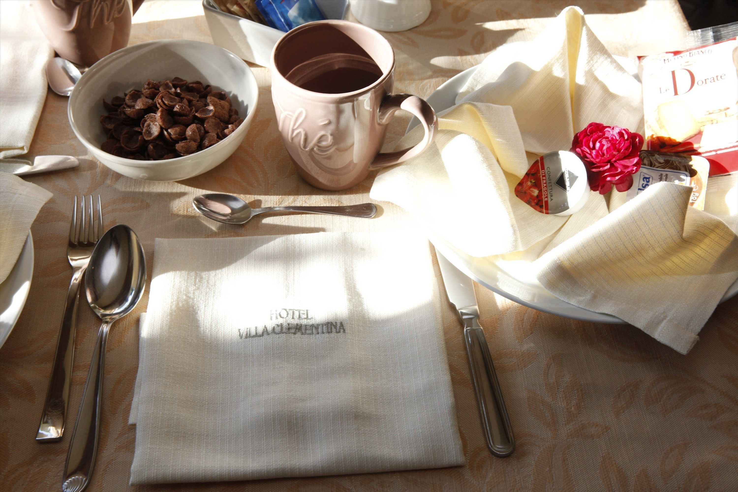 A table set with a bowl of cereal, a mug, cutlery, a napkin, and a small bouquet of flowers.