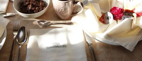 A table set with a bowl of cereal, a mug, cutlery, a napkin, and a small bouquet of flowers.