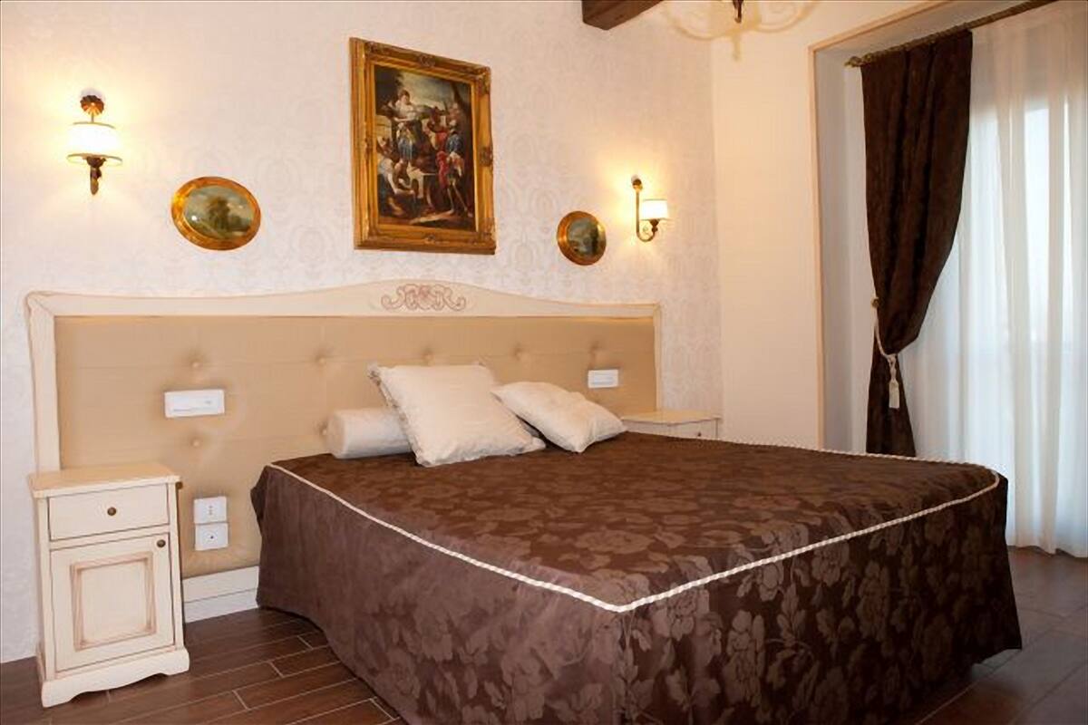 Une chambre à coucher avec un grand lit, une table de chevet, un tableau accroché au mur et deux appliques murales.