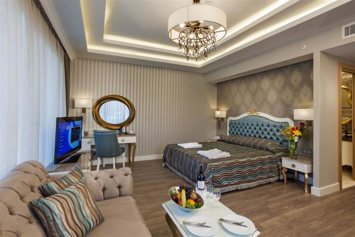 A modern hotel room with a large bed, a sofa, a desk, and a television.