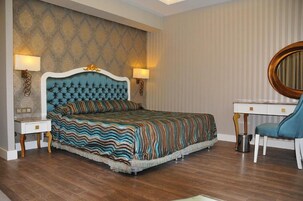 Un dormitorio con cabecera capitonada, colcha a rayas, lámparas de noche, un espejo redondo y un escritorio con silla.