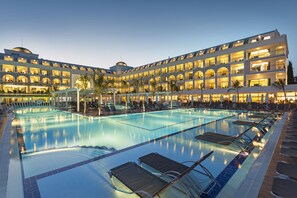 Ett hotell med en stor swimmingpool, flera balkonger och en väl upplyst fasad.
