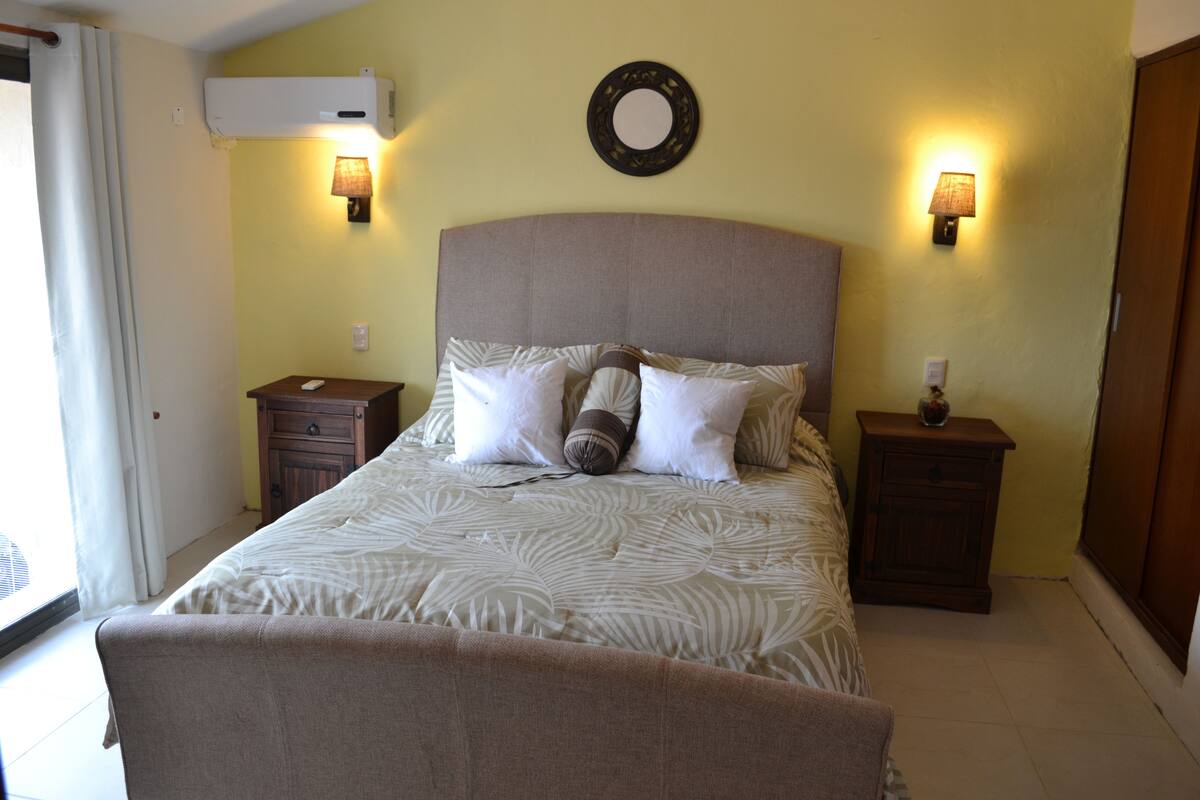 Un dormitorio con una cama grande, dos mesitas de noche, un espejo en la pared y un equipo de aire acondicionado.