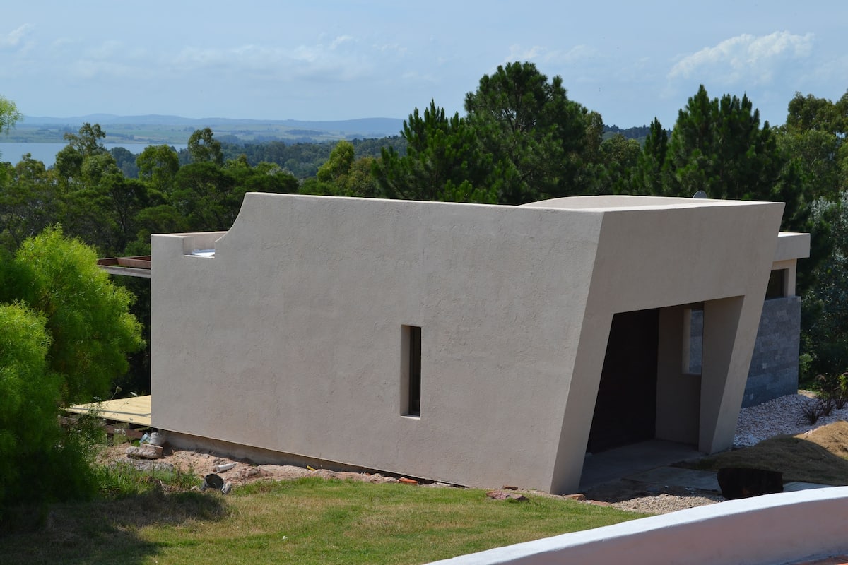 Un edificio moderno con techo plano, una ventana pequeña y vistas a un lago y montañas.
