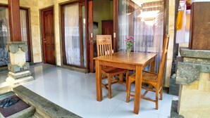 A wooden dining table with chairs, a vase with flowers, and a stone staircase leading to an entrance. - Uma Dewi Guest House (Ubud)