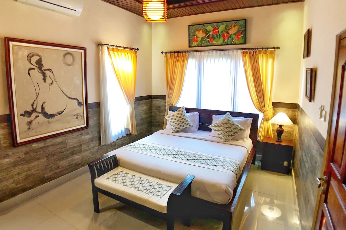 A bedroom with a bed, a nightstand, a lamp, a painting, and a ceiling fan.