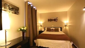 A hotel room with a bed, a desk, a lamp, and a wall-mounted picture. - Le Figuier (Ivry-sur-Seine)