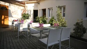 An outdoor patio with white chairs and tables, surrounded by potted plants and a tiled floor. - Le Figuier (Ivry-sur-Seine)