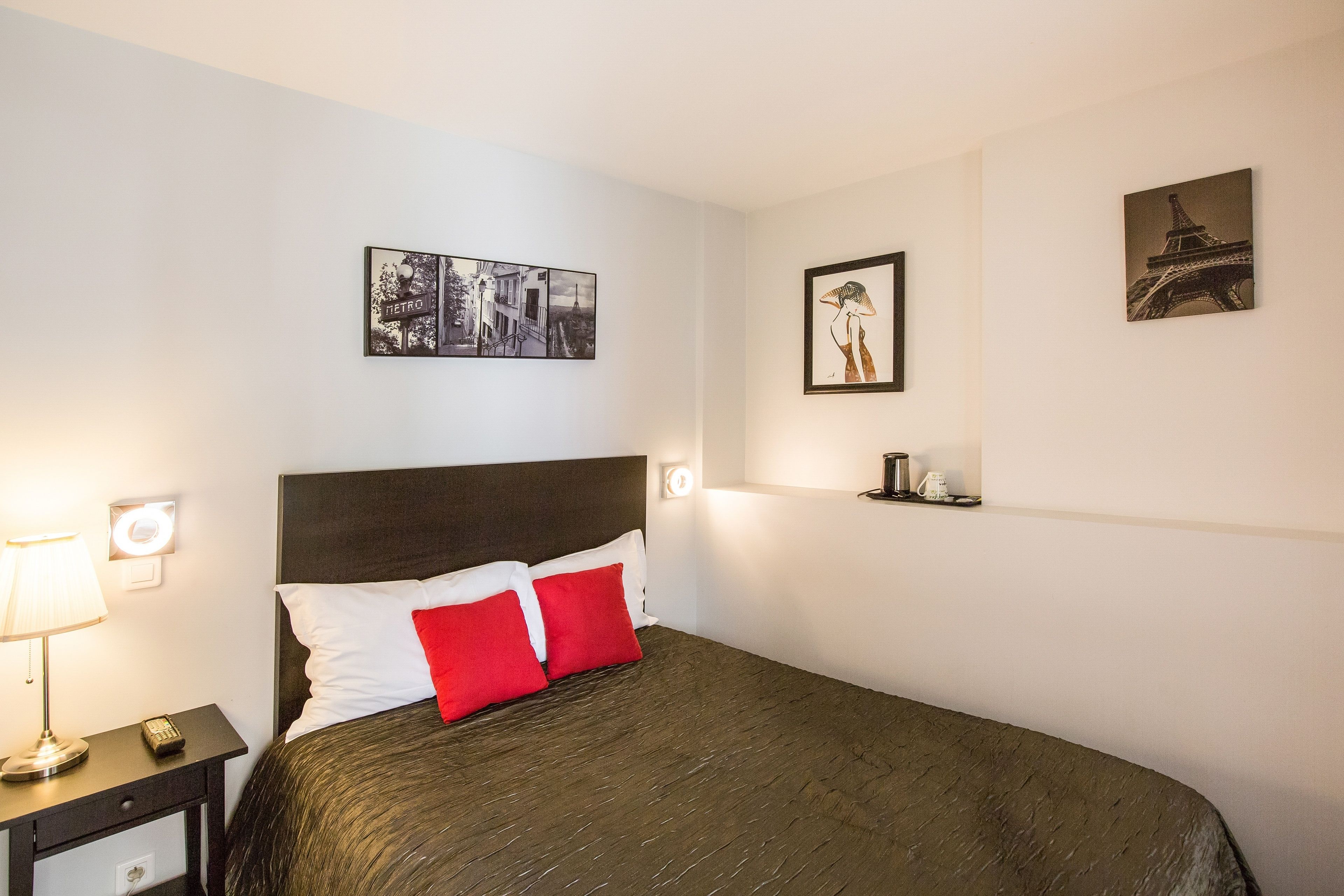 A hotel room with a bed, a nightstand, a lamp, and wall art including a metro scene and the Eiffel Tower.