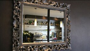 A mirror with an ornate frame reflecting a bar area with shelves of bottles. - Le Figuier (Ivry-sur-Seine)