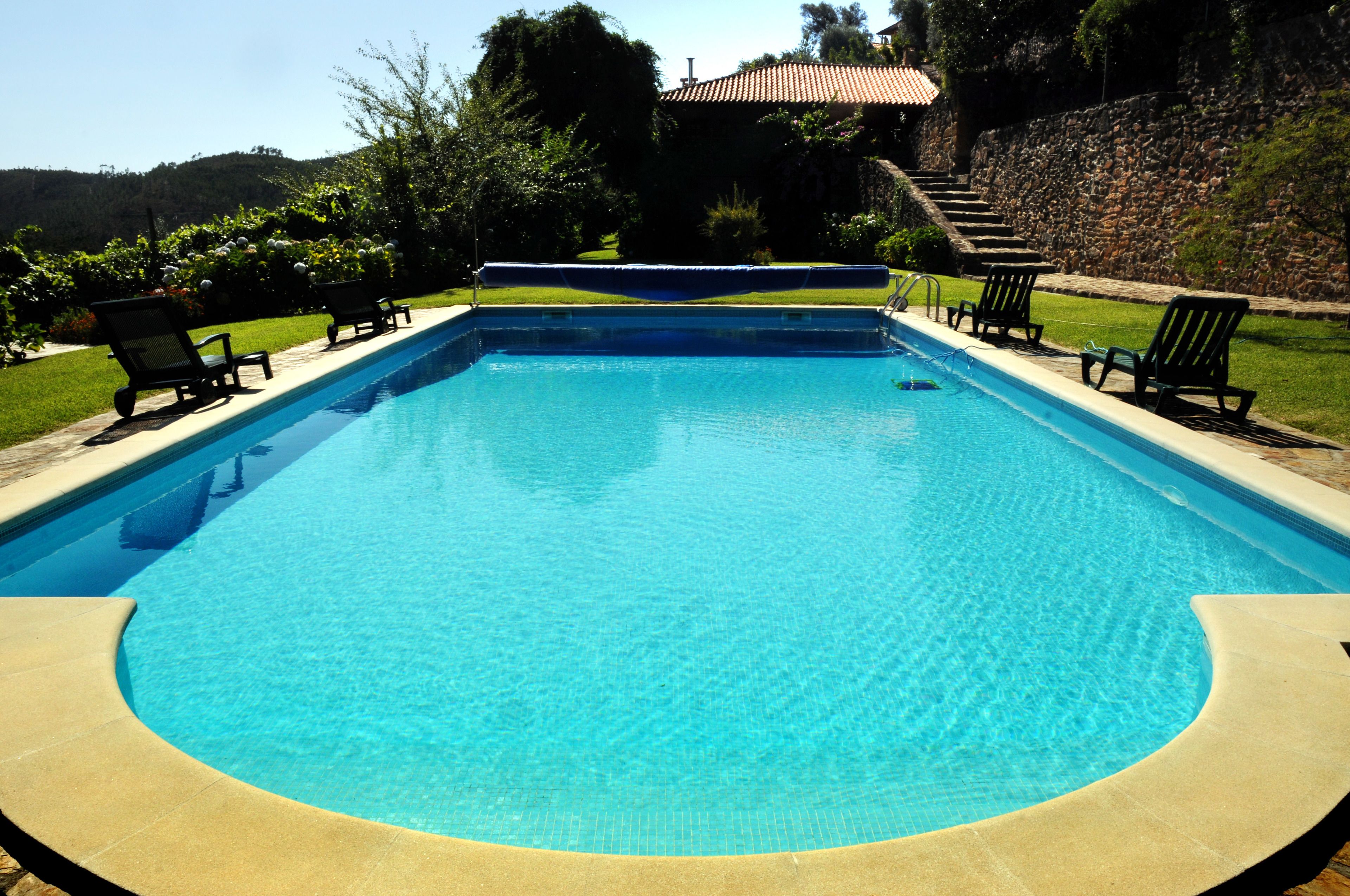 A rectangular swimming pool with a clear blue water surface, surrounded by a stone wall and a grassy area with several lounge chairs.