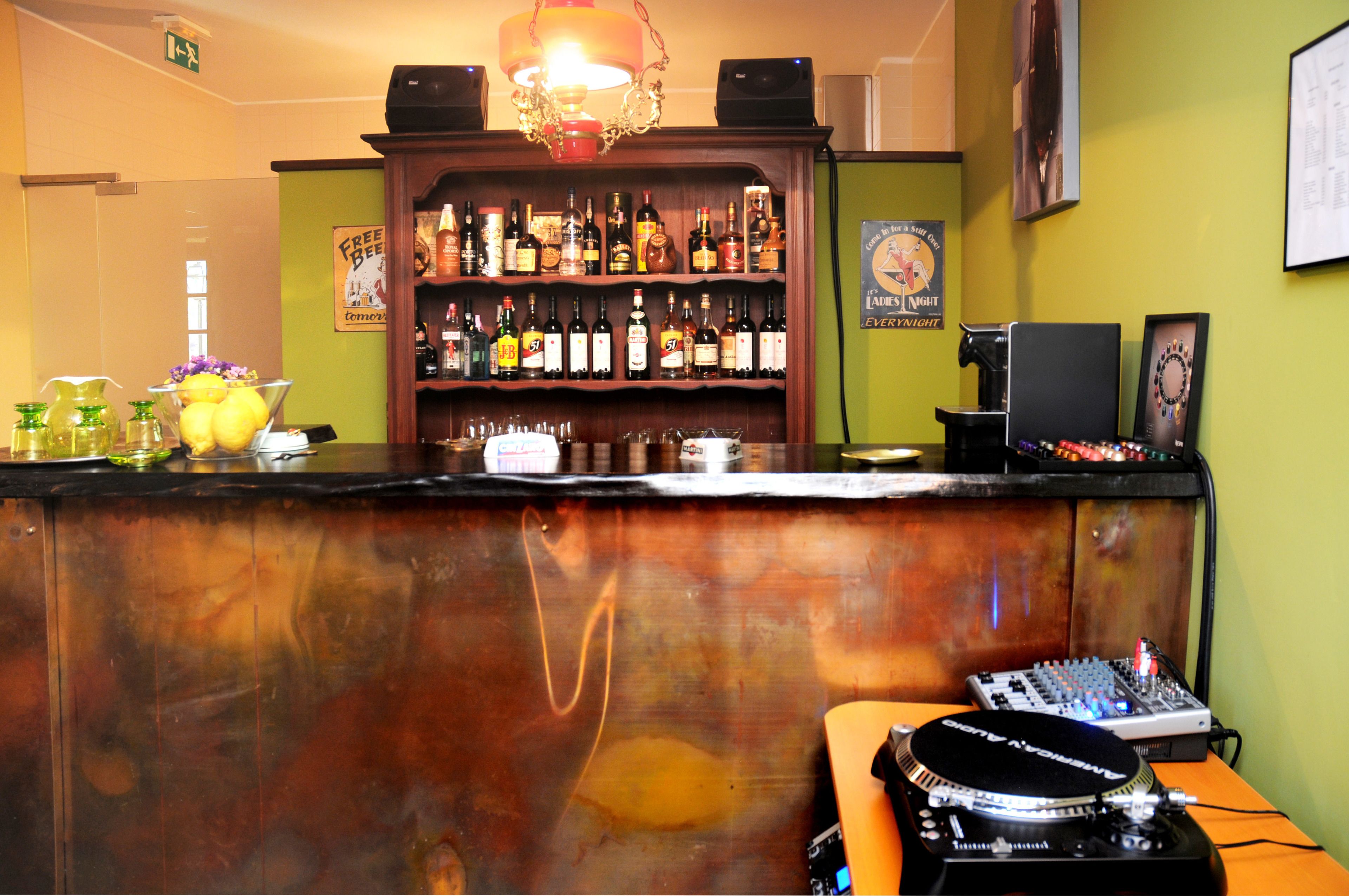 Eine Bar mit Holztresen, Regalen voller Spirituosen, einer DJ-Anlage und einer dekorativen Leuchte.