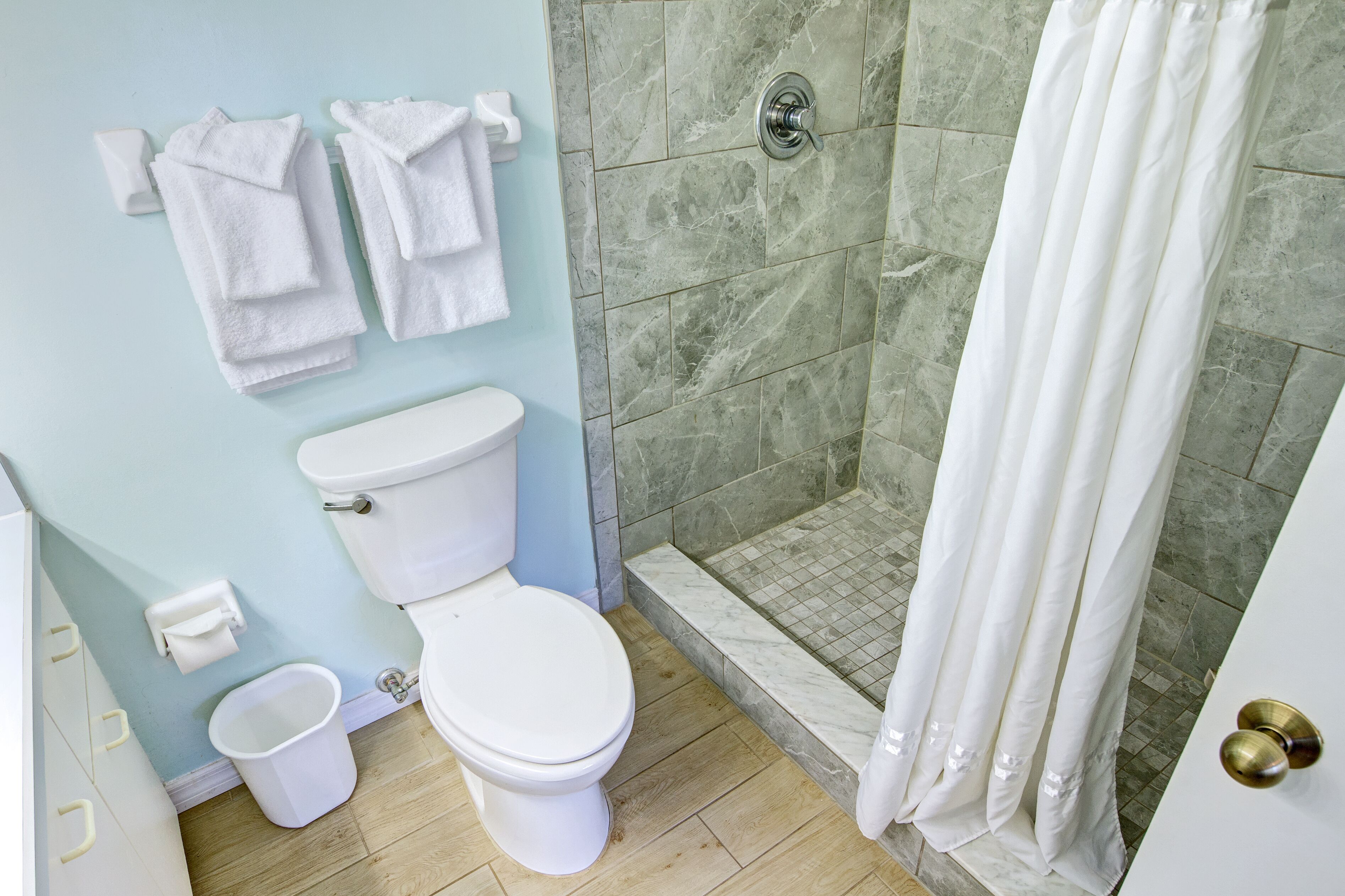A bathroom with a toilet, a shower with a glass door, and a towel rack with towels.