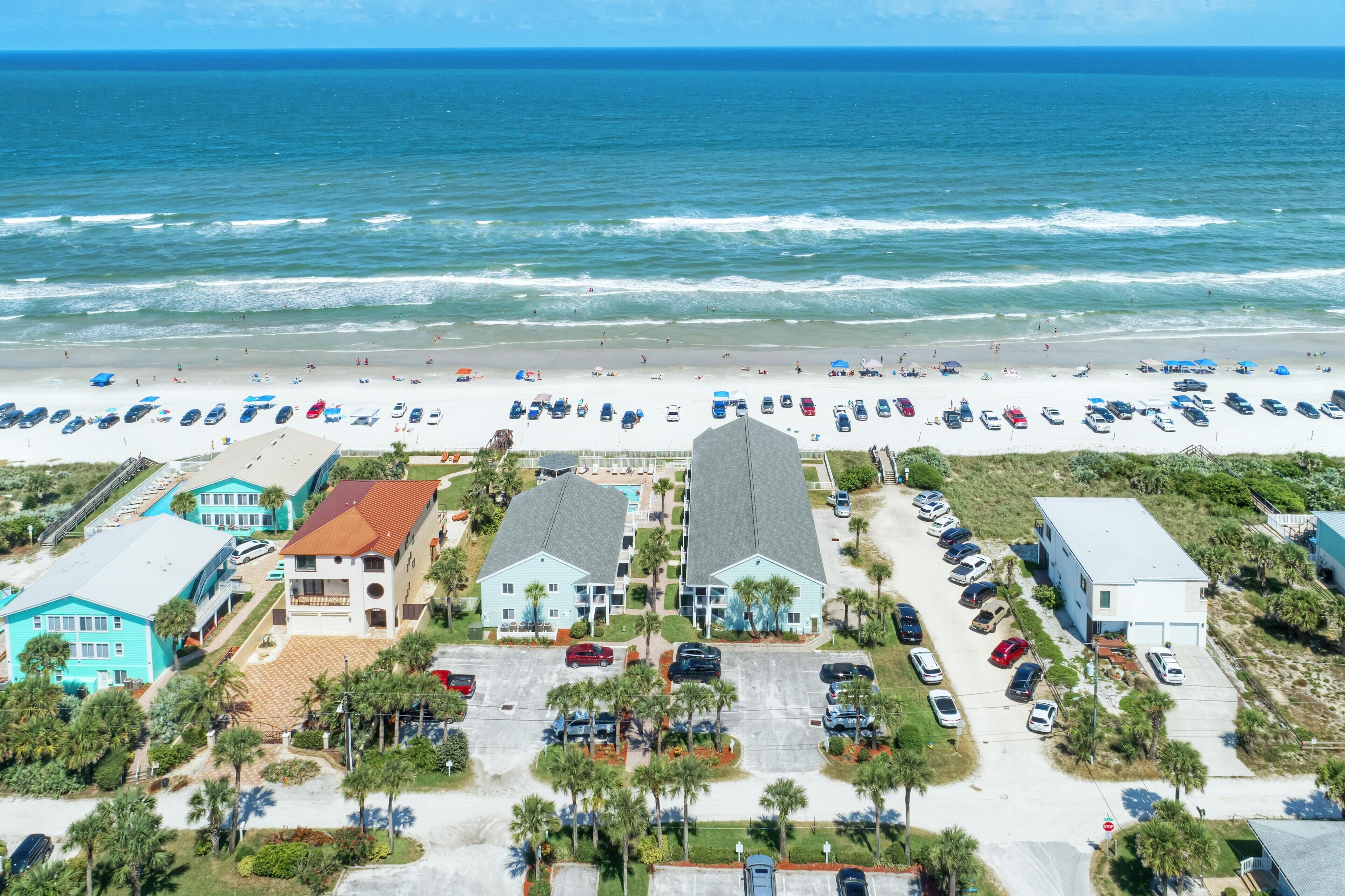 A beachfront hotel with multiple buildings, parking lots, and a beach in the background.