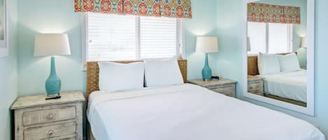 A bedroom with a large bed, two nightstands, a mirror, and a window with blinds.