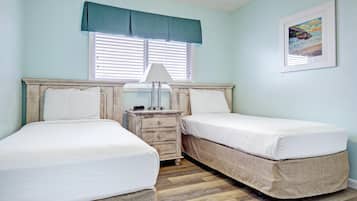Une chambre avec deux lits, une table de chevet, une lampe et une fenêtre avec des stores.