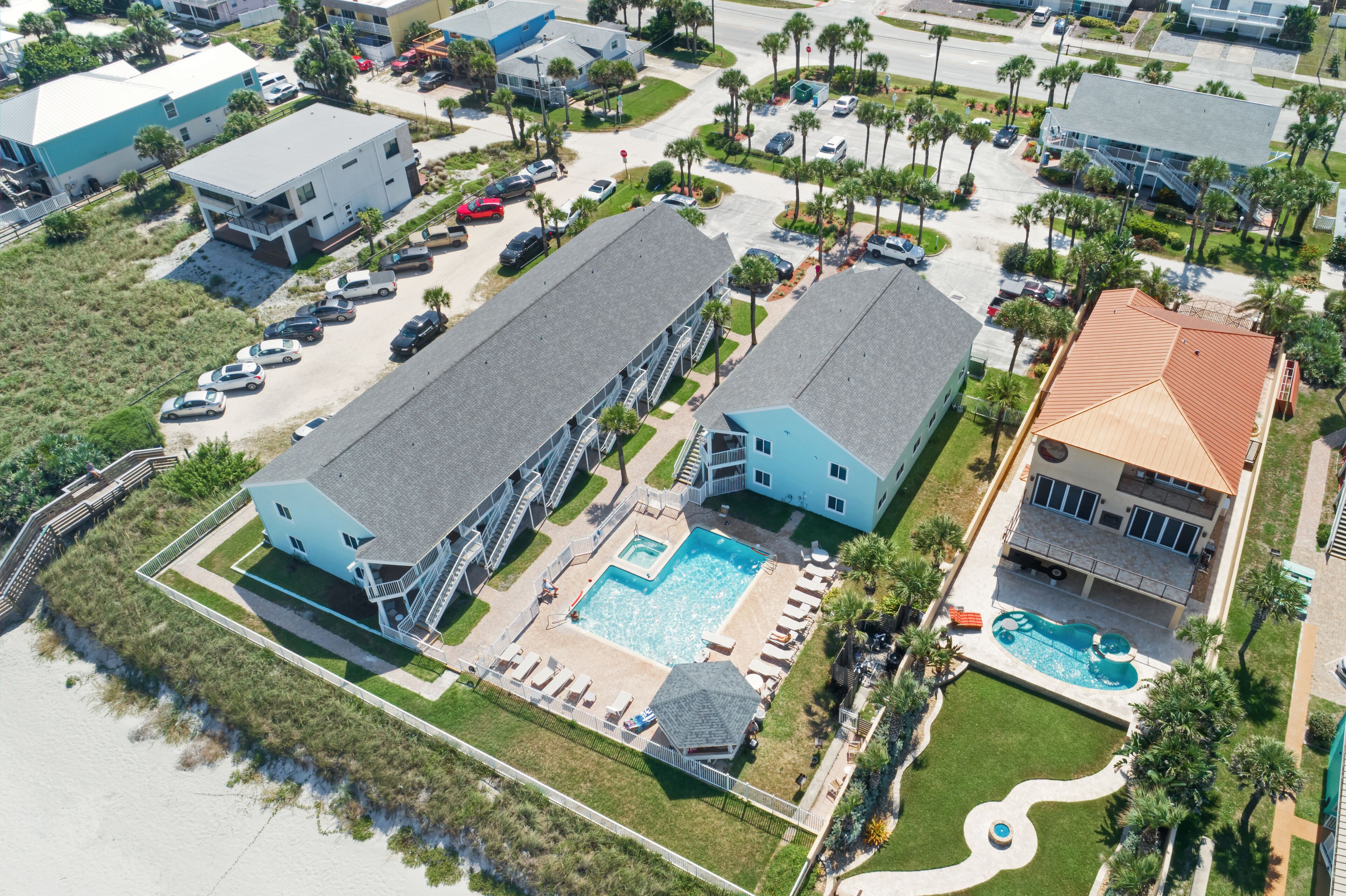 Una vista aerea di una zona residenziale con due grandi case, una piscina e una spiaggia.