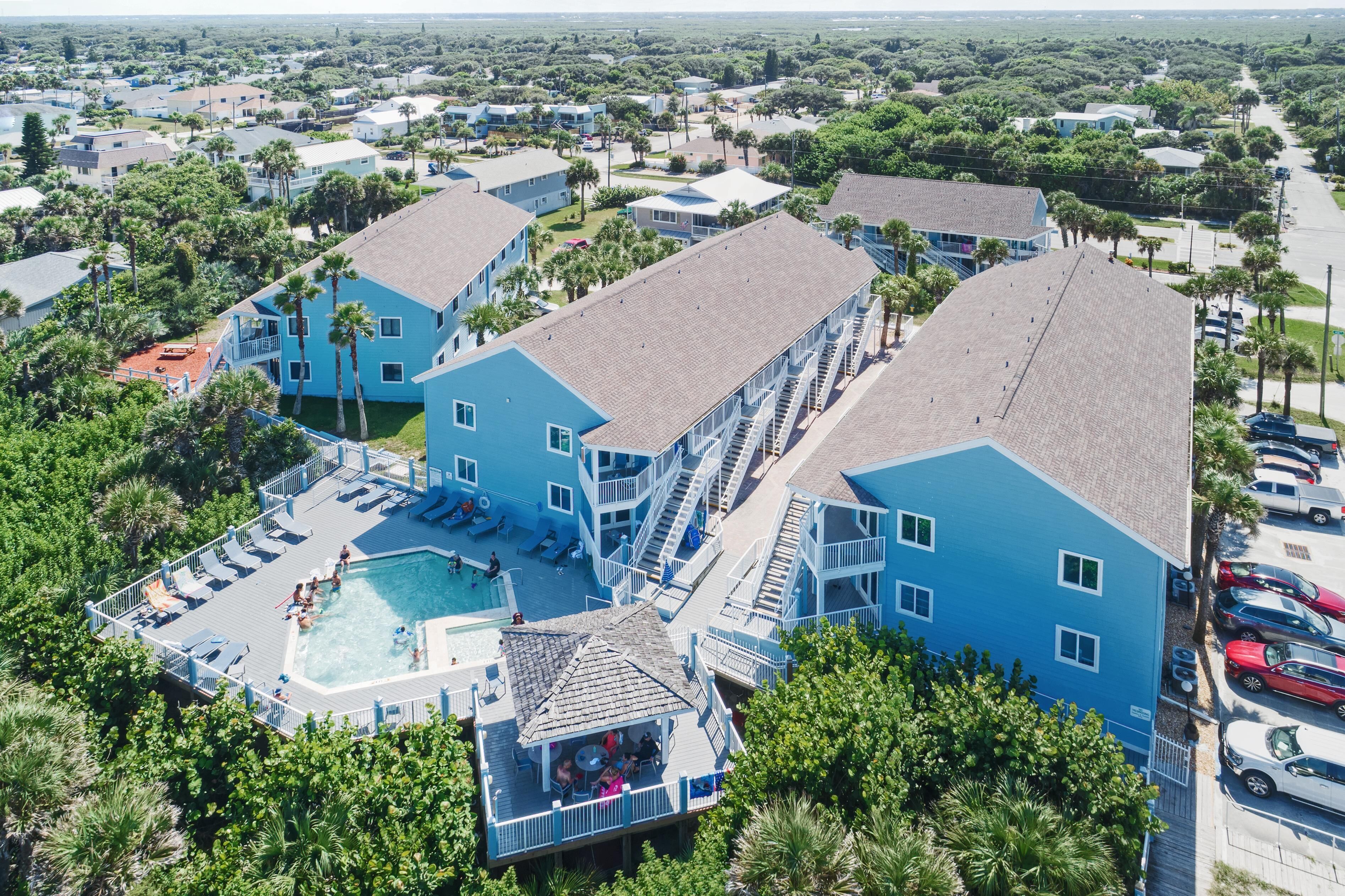 A resort with multiple blue buildings, a central swimming pool, and a parking area.