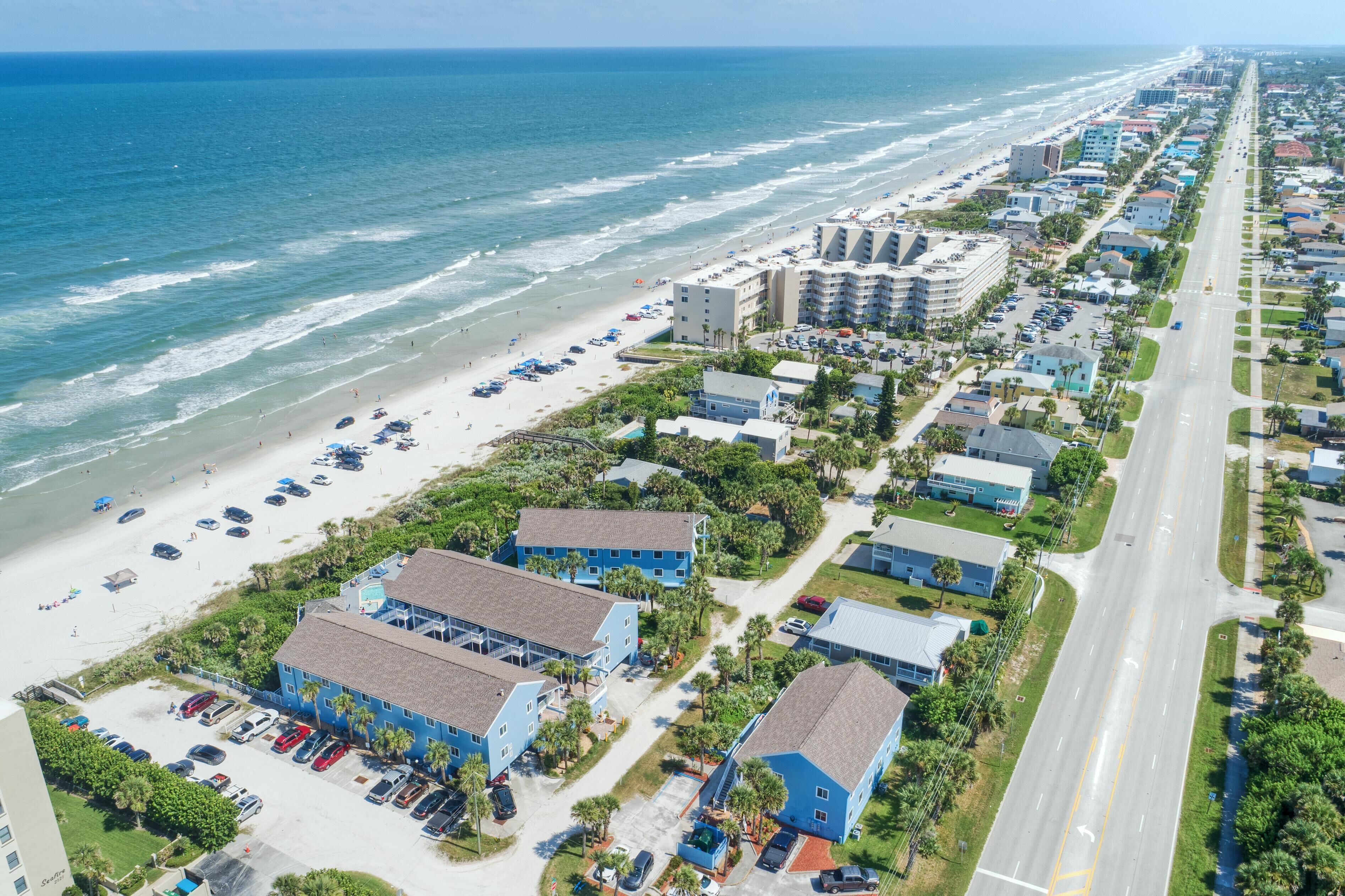 A coastal hotel with multiple buildings, a beach, and a road.