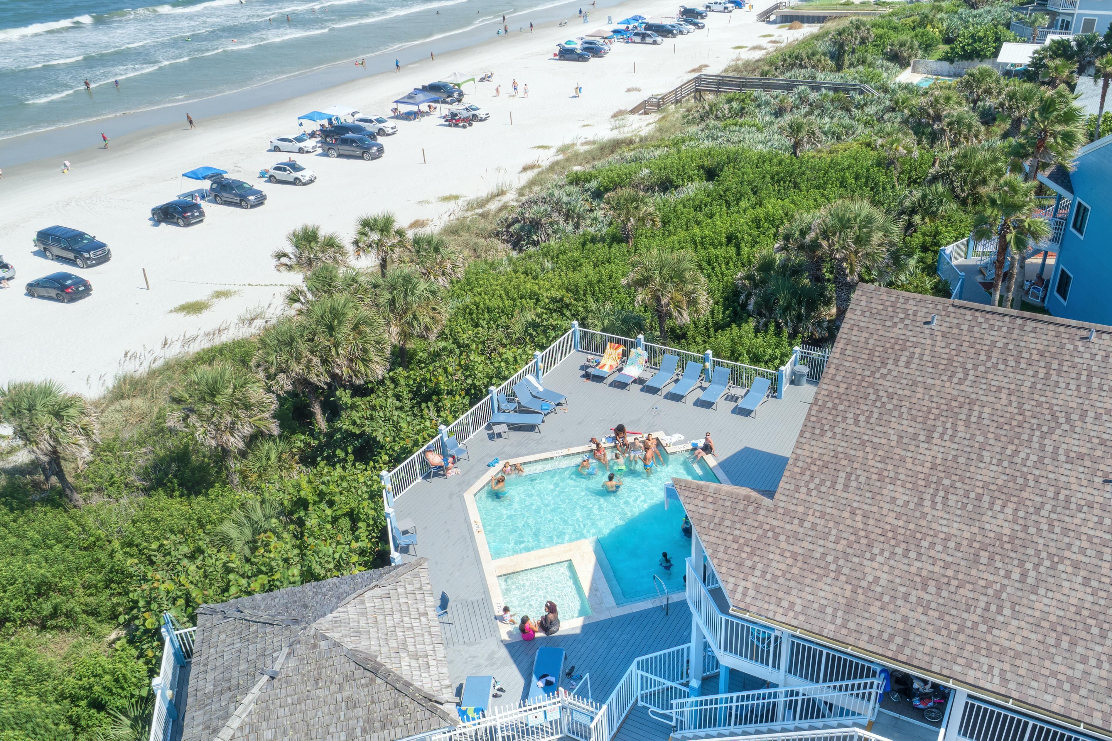 A pool area with a view of the beach and parked cars.