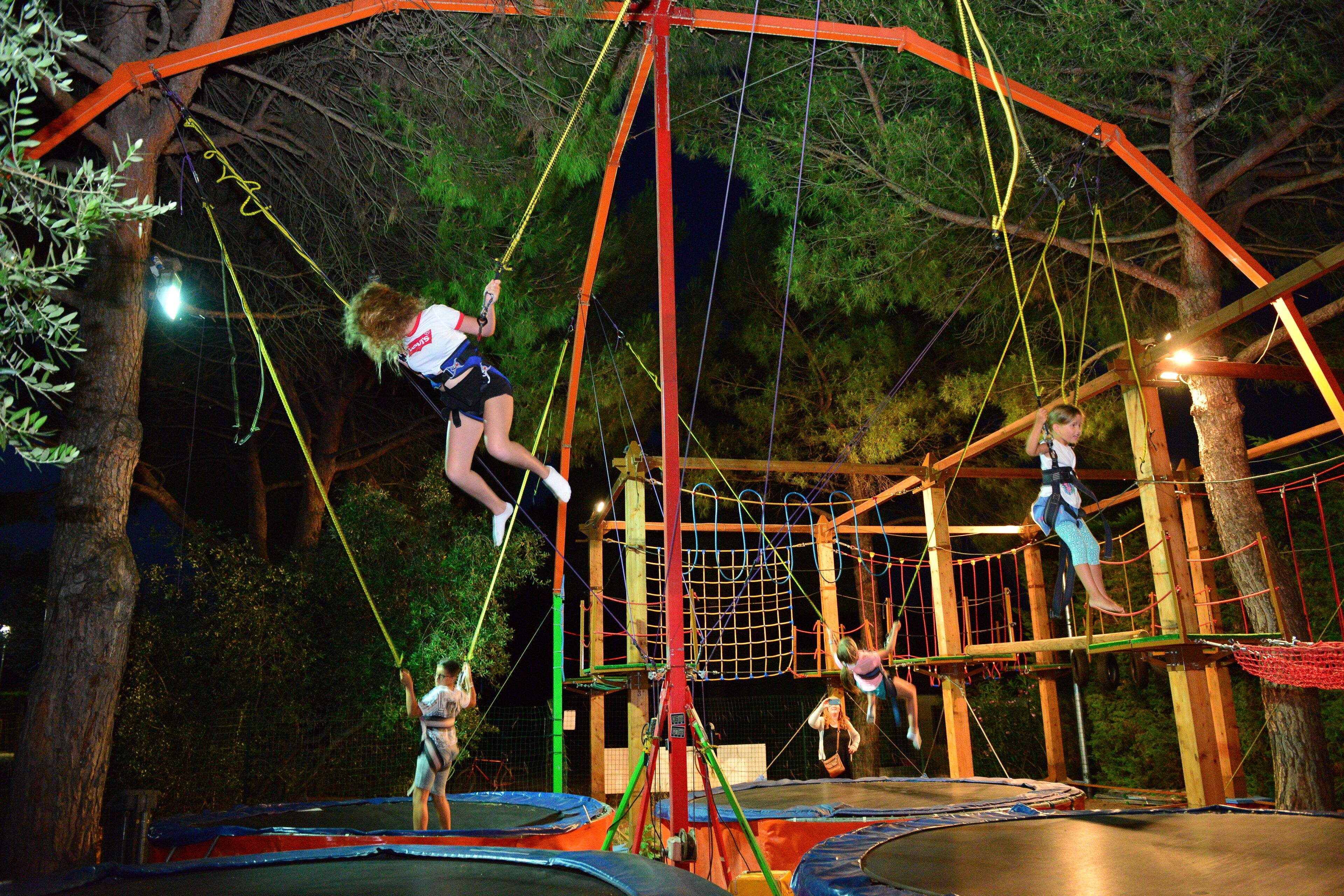 Un parque de aventuras nocturno al aire libre con puentes colgantes, trampolines y una zona de escalada con redes.