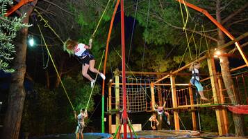 Un parc d’aventure en plein air, ouvert la nuit, avec des ponts de cordes, des trampolines et une zone d’escalade avec des filets.
