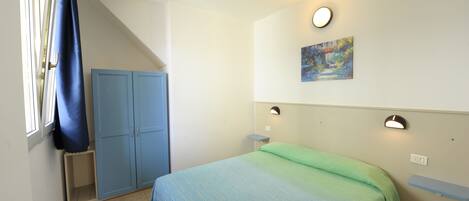 A bedroom with a bed, a wardrobe, a painting, and a window with curtains.