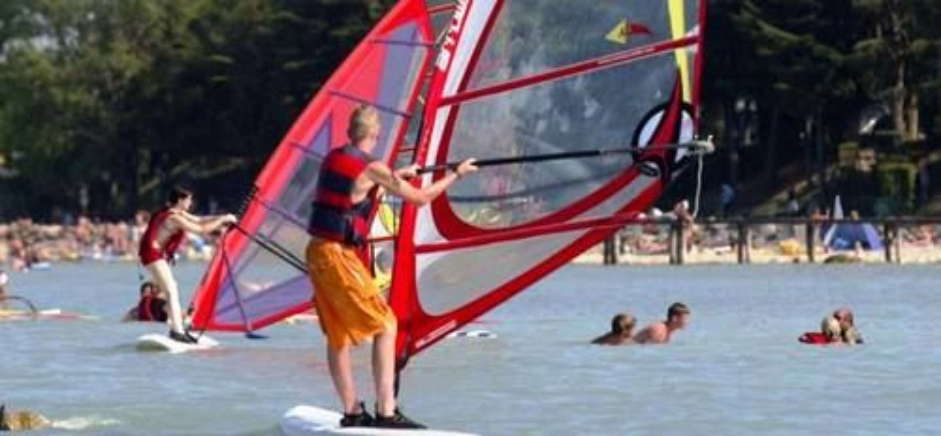Una persona practica windsurf en un lago, con otras actividades de windsurf al fondo.