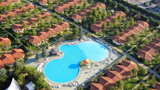 Vista aérea de um bairro residencial com casas uniformes de telhado vermelho, uma piscina central e um toboágua.