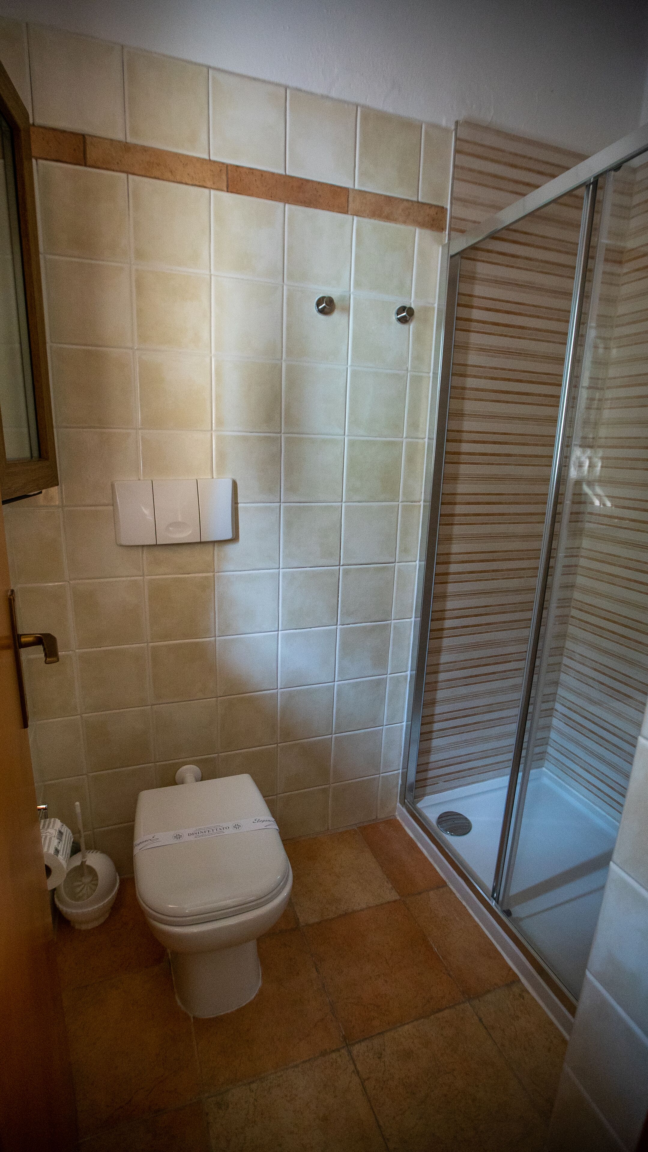 Un bagno con il water, una doccia con porta in vetro e un portasciugamani per la carta igienica.