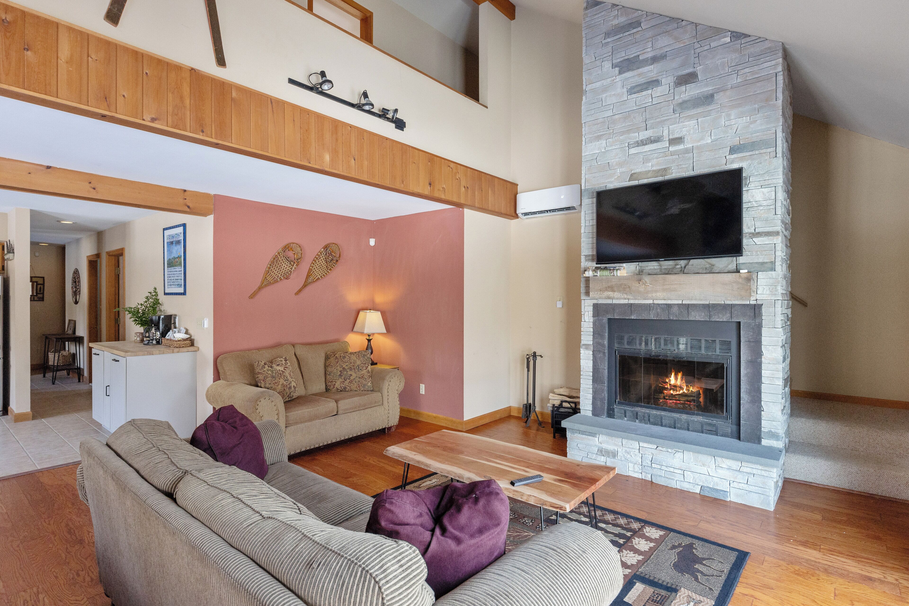 Amplia sala de estar con chimenea de piedra, un televisor de pantalla plana grande y un techo alto con vigas de madera a la vista.