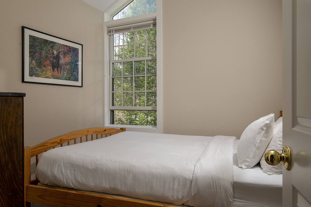 Un dormitorio con una cama individual, una ventana con vistas a árboles y un cuadro en la pared.