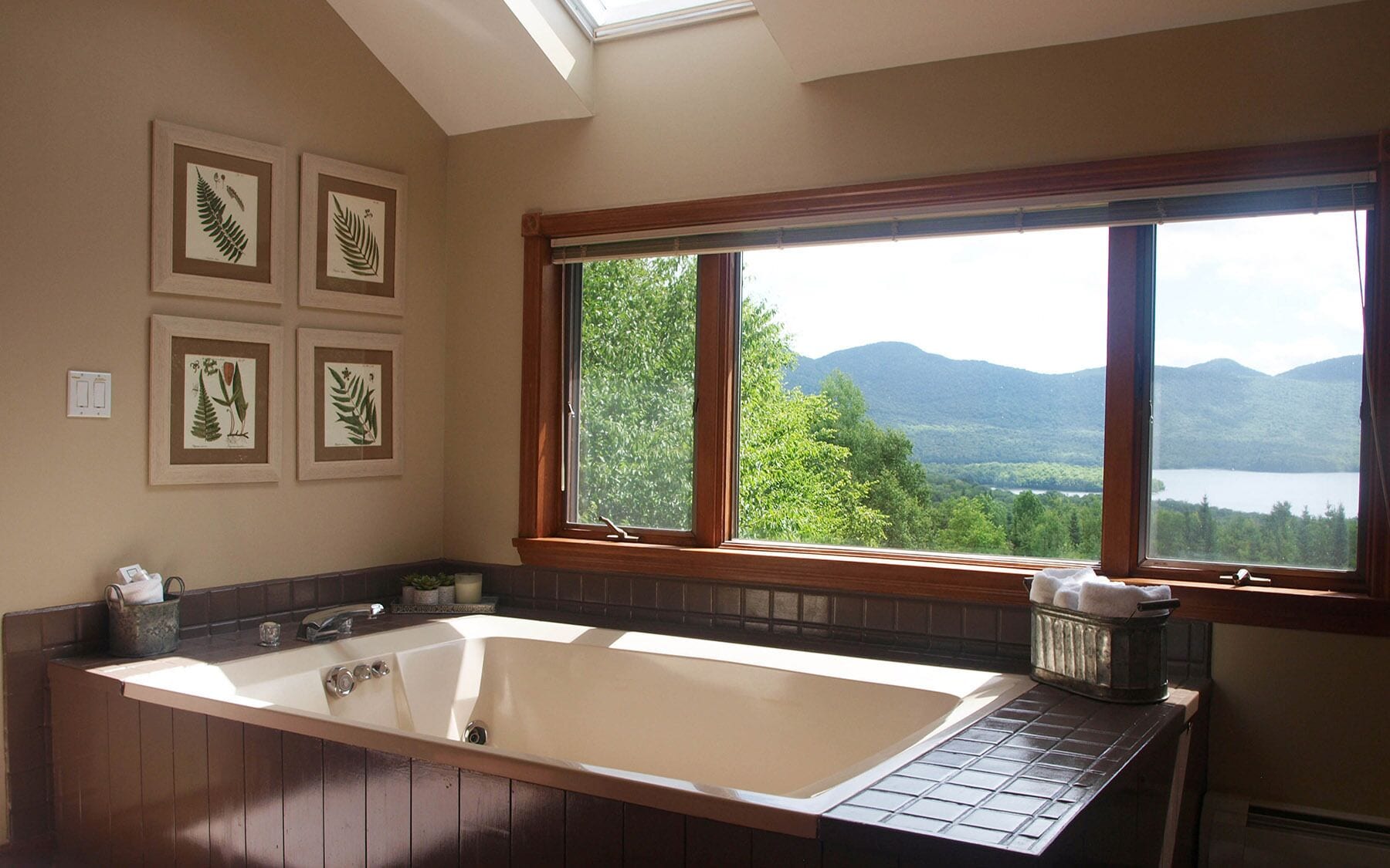 Une salle de bain dotée d’une grande baignoire, d’une fenêtre offrant une vue sur les montagnes et un lac, et de reproductions botaniques encadrées accrochées au mur.