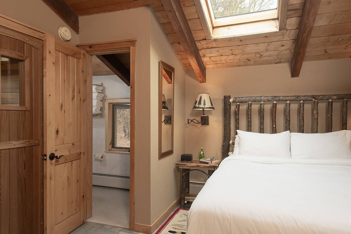 Un dormitorio con cabecera de madera, una cama, una mesita de noche, una lámpara y una ventana.