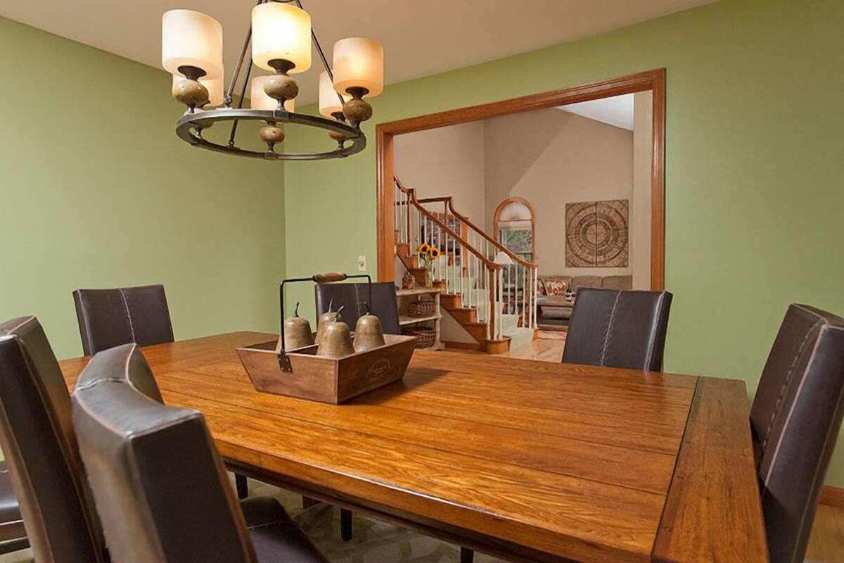 Un comedor con una mesa y sillas de madera, un candelabro y una escalera que conduce a otra habitación.